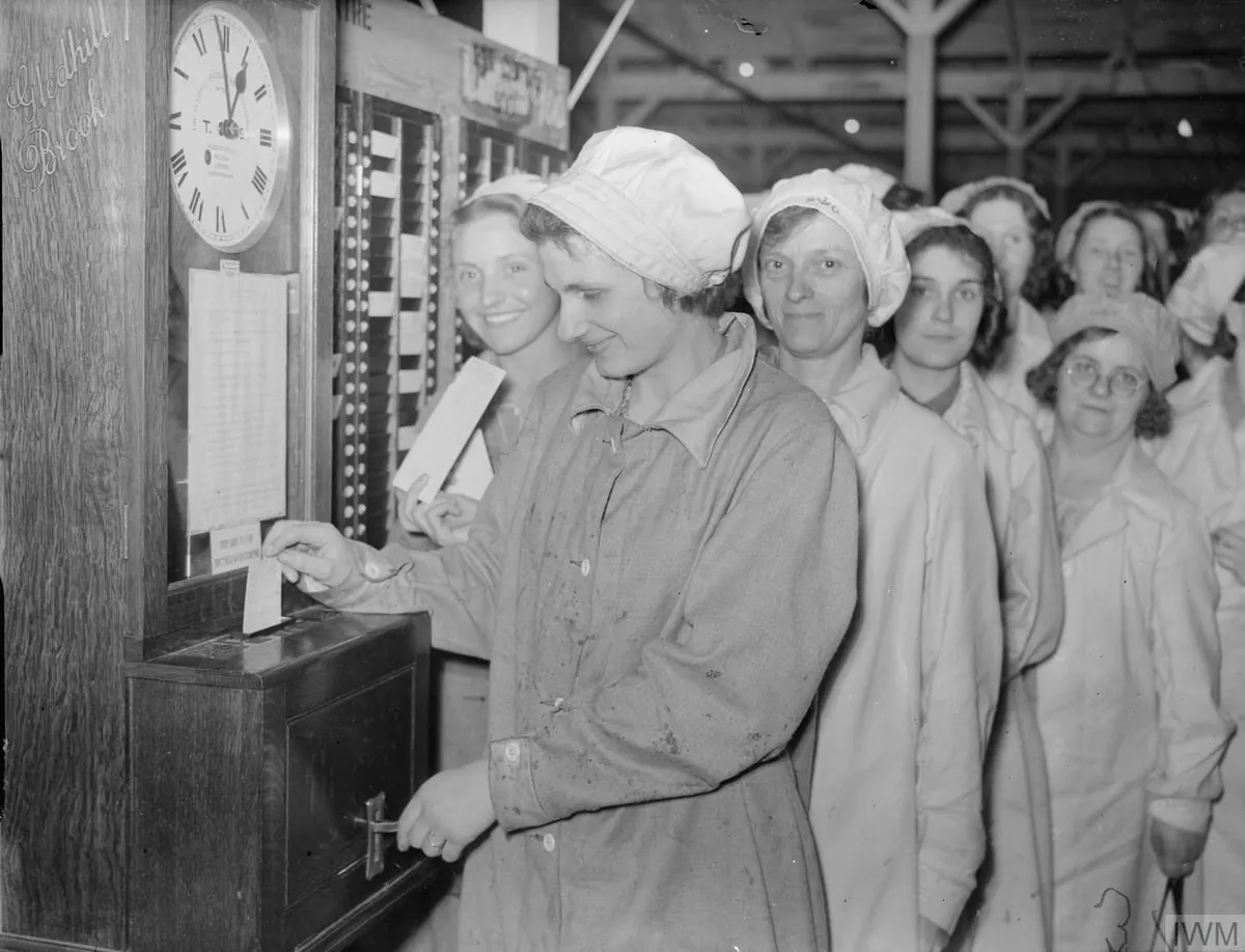 A wartime British factory worker clocking in at a time recorder on the wall, card in hand.