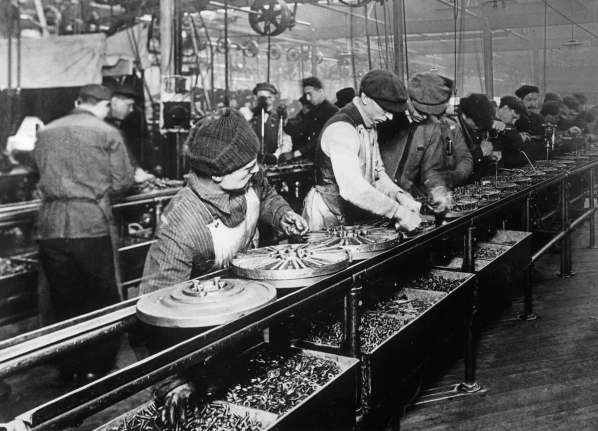 The Ford assembly line in 1913: a chassis moving between rows of workers, each fitting one part.