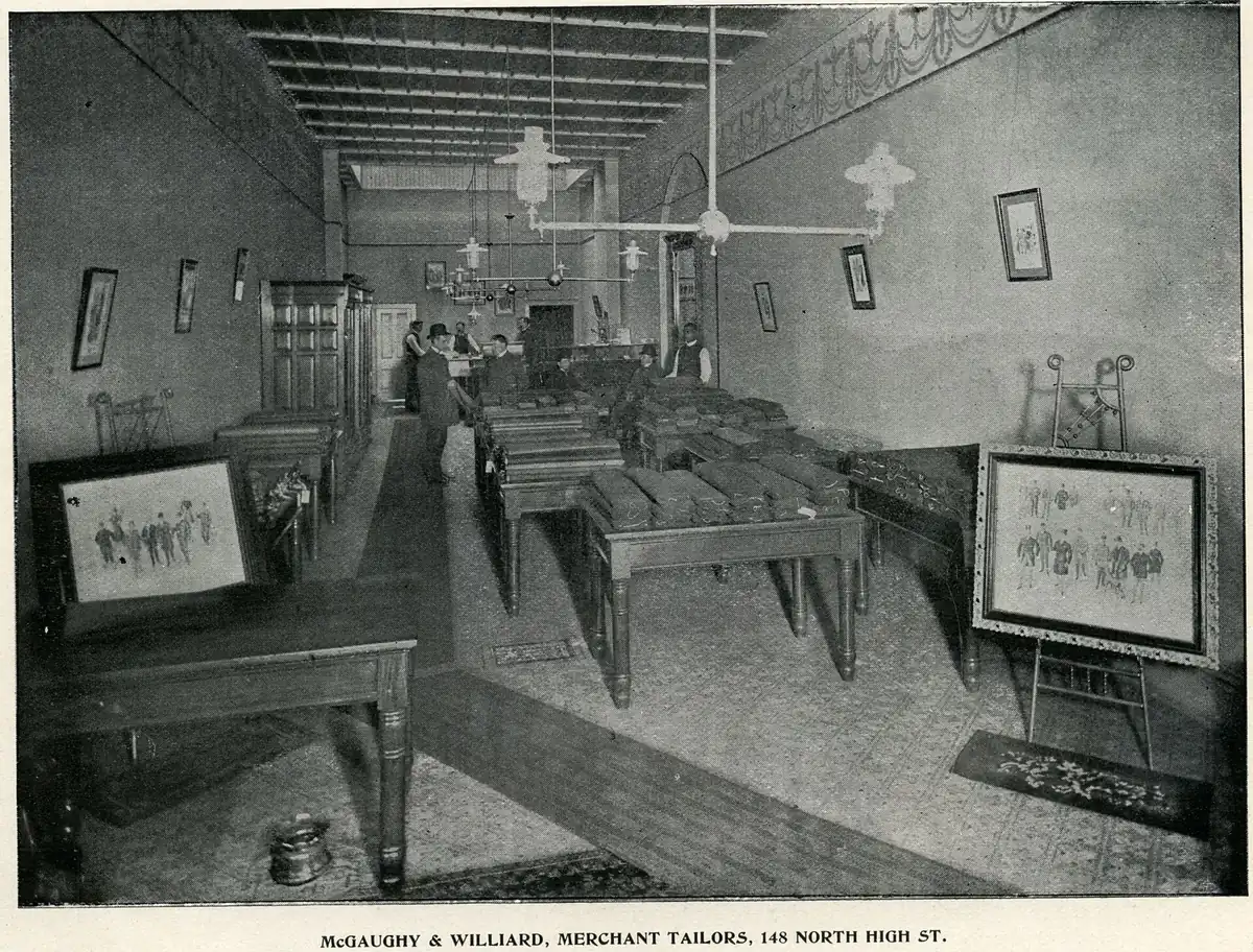 The interior of McGaughy & Williard, merchant tailors: staff at work benches, stock on shelves, a counter at the front.