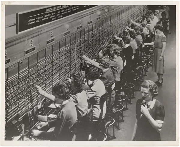 A row of women working at a Bell System telephone switchboard, headsets on, patching calls by hand.